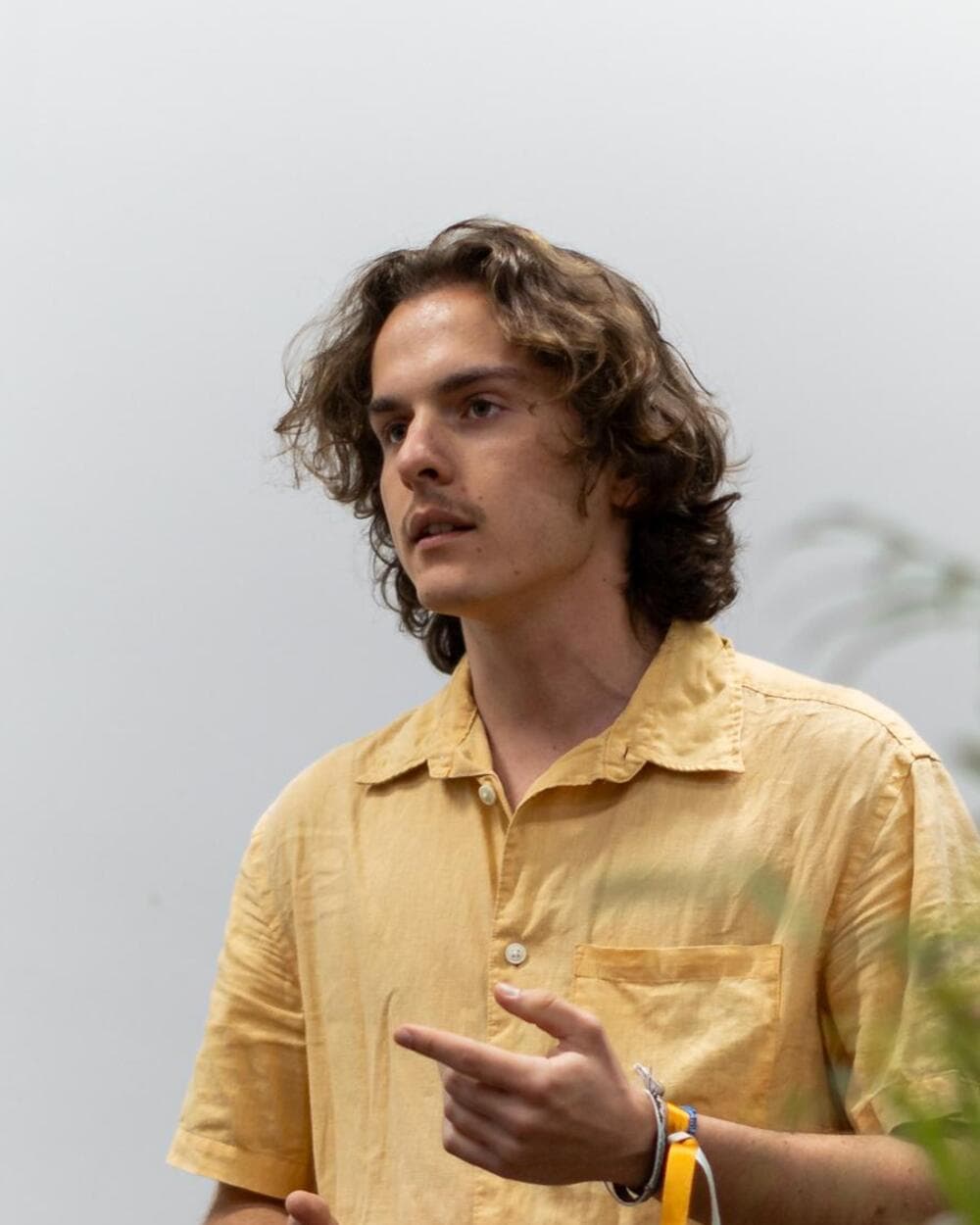 David presenting in a yellow linen shirt, gesturing at something off-frame.